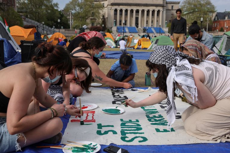 students paint a banner in front of a stately building 